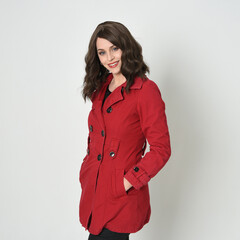 Wall Mural - close up portrait of beautiful brunette woman model, wearing red trench jacket.isolated on white studio background. posing with  hands in pocket of jacket.