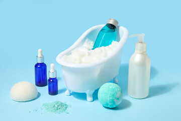 Wall Mural - Composition with mini bathtub, bottles of cosmetic products and bomb on blue table near wall