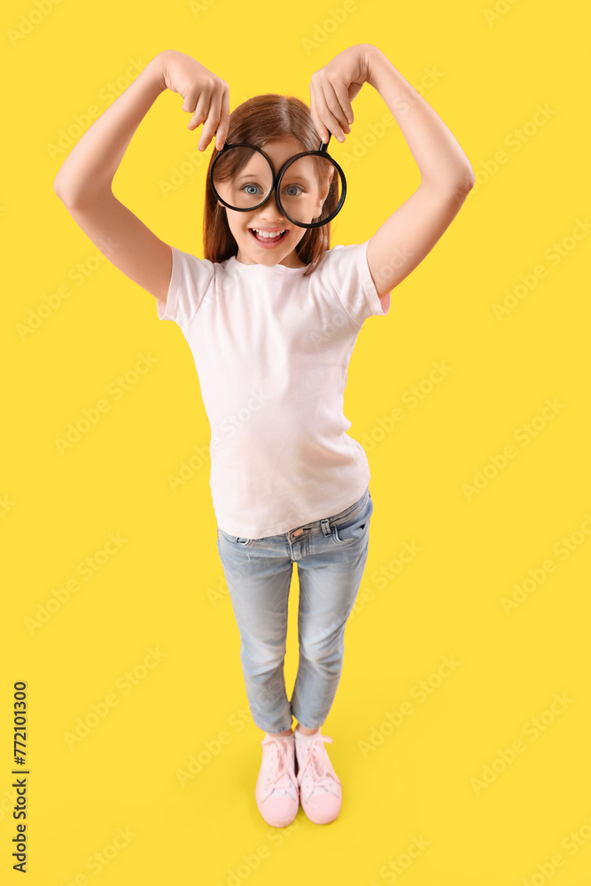 Funny little girl with magnifiers on yellow background