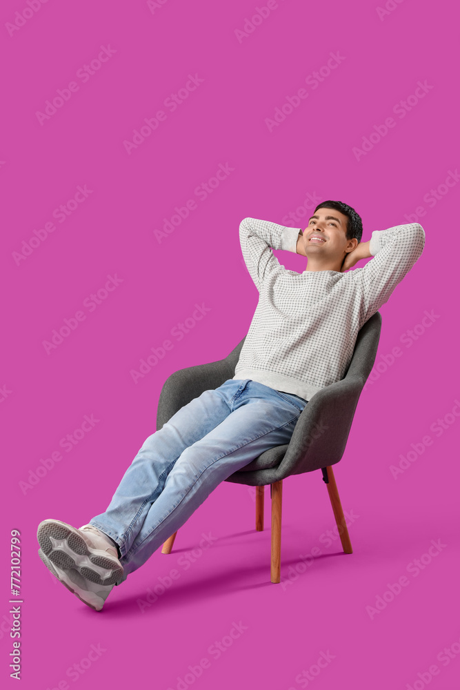 Young man sitting in armchair on purple background