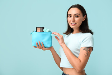 Sticker - Beautiful young woman with cosmetic bag full of makeup products on blue background