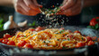 Close-up of a professional cook's hands sprinkling fine herbs over a steaming dish of linguine with marinara, surrounded by fresh tomatoes and garlic on the counter