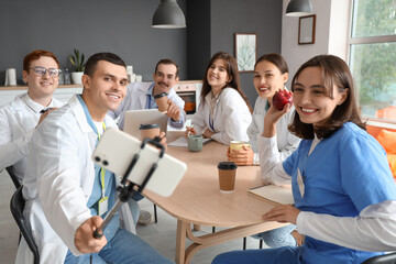 Wall Mural - Team of doctors taking selfie on coffee break at table in hospital kitchen