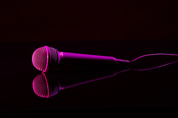 Wall Mural - Modern microphone on glass table against dark background