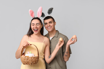 Wall Mural - Happy young couple with Easter basket and bunny ears on grey background