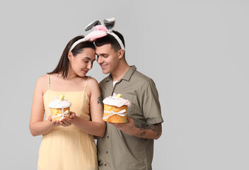 Wall Mural - Happy young couple with Easter cakes and bunny ears on grey background