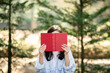 © Prostock-studio - A person is holding a red hardcover book in front of their face