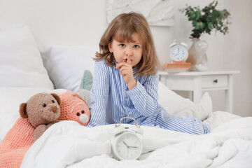 Poster - Adorable little girl with plush toys and alarm clock showing silence gesture on bed