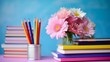 A vase of pink flowers sits on a desk next to a stack of books