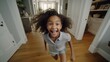 A young girl with curly hair is running through a room. She is smiling and she is happy