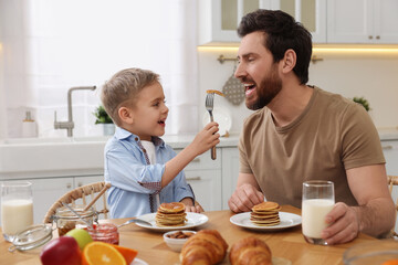 Canvas Print - Father and his cute little son having breakfast at table in kitchen