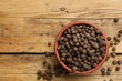 Aromatic allspice pepper grains in bowl on wooden table, top view. Space for text