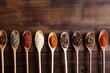 Spices on wooden spoons are displayed in a row on a dark wooden background. Top view