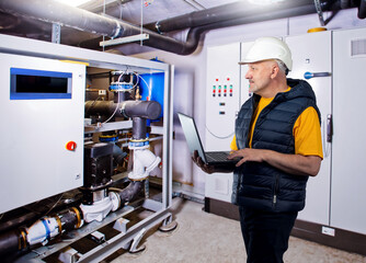 Poster - Man inspects boiler equipment. Engineer in factory basement. Engineering room with boiler equipment. Industrial worker. Man with laptop in boiler room. Inspector inspects technical room supermarket