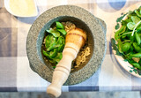 Fototapeta Boho - Preparation of traditional Pesto alle Genovese - with basil, olive oil, pine nuts, parmesan cheese and garlic crush in a mortar with a wooden pestle