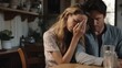 © liliyabatyrova - Unhappy young family facing troubles. Crying wife covering face with her hand and her sad husband hugging supporting each other in grief sitting at table in kitchen.