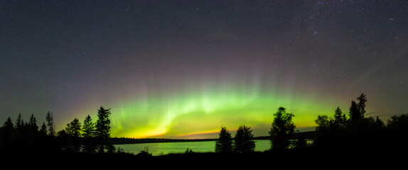 bright green aurora arc across the sky above a lake with pine trees in the foreground. the lake refl