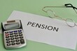 The word Pension on a piece of paper on green background  with a calculator and glasses. The concept of pension payments to pensioners.