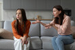 © Home-stock - Annoyed mother gesturing to teen daughter sitting on couch, sad teen girl looking away, relationship problems with teenagers and generation gap concept