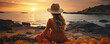 Young woman in hat sitting on the sand and looking at the sea at sunset. Solo travel, vacation concept.