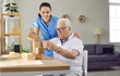 © Studio Romantic - Helpful nurse playing games with old male patient. Senior man with cognitive disorder building wooden block tower while sitting at table in retirement home. Dementia care, Alzheimer's disease concept