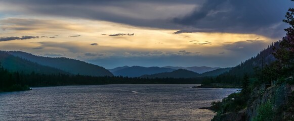 Wall Mural - Picturesque landscape of a river with a mountain range illuminated by the setting sun