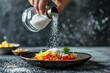 A person delicately sprinkles salt onto a plate of food, adding a finishing touch of flavor