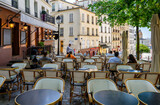 Fototapeta Paryż - Cozy street with tables of cafe in quarter Montmartre in Paris, France. Architecture and landmarks of Paris. Postcard of Paris
