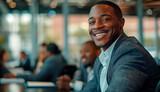 Fototapeta  - A charismatic African American businessman with a captivating smile sits in a lively office environment, reflecting a persona of friendliness and professionalism.