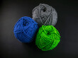 Three balls of yarn are sitting on a black background. The balls are of different colors, with one being blue, one being green, and one being gray. Concept of creativity and craftsmanship