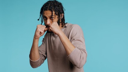 Middle Eastern man pretending to fight, throwing punches, holding defensive guard. BIPOC martial artist person mock boxing, holding combat stance, exercising in blue studio background, camera B