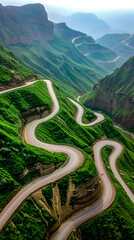 Wall Mural - Aerial view of winding road surrounded by green mountains and greenery.