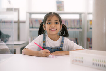 Wall Mural - A young girl is sitting at a desk with a red crayon in her hand