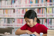 © FAMILY STOCK - A girl is sitting at a table in a library, reading a book