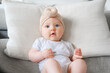 Caucasian female infant dressed in bodysuit and turban on sofa. Surprised face. Infant emotions and expressions.
