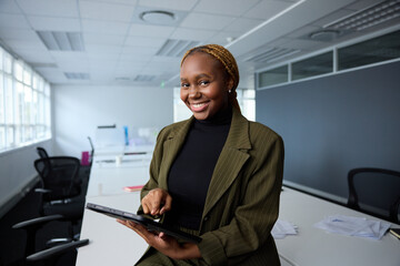 Wall Mural - Confident young black businesswoman in businesswear using digital tablet by desk in office