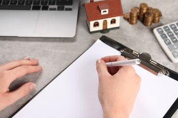 Wall Mural - Woman planning budget, closeup. House model and coins on grey table