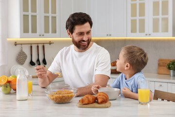 Canvas Print - Father and his cute little son having breakfast at table in kitchen