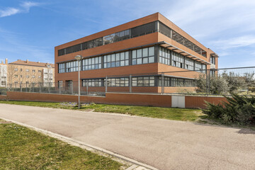 Wall Mural - Terracotta brick and black metal facade of office building with a landscaped walkway outside the perimeter fence