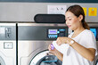 Asian woman pouring liquid detergent into washing machine. 