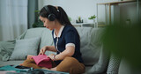 Fototapeta Mapy - Selective focus of Asian teenager woman wear wireless headphones sitting on sofa packing travel luggage with clothes for traveling trip, Preparation travel suitcase at home.
