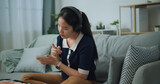 Fototapeta Mapy - Selective focus of Asian teenager woman wear wireless headphones sitting on sofa making checklist of things to pack for travel, Preparation travel suitcase at home.