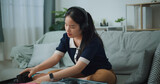 Fototapeta Mapy - Selective focus of Asian teenager woman wear wireless headphones sitting on sofa packing travel luggage with personal items for traveling trip, Preparation travel suitcase at home.