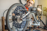 Fototapeta  - A male bicycle mechanic repairs a mountain bike in a workshop. The concept of preparation for the new season, repair and maintenance