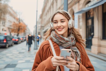 Wall Mural - Caucasian young woman is listening to music on smartphone with headphones outdoors