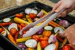 person using silicone tongs to turn vegetables on a roasting pan