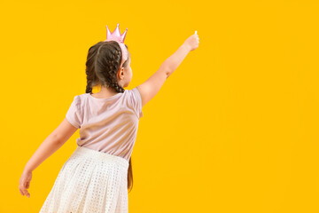 Wall Mural - Little girl in crown with chalk piece on yellow background, back view. Children's Day celebration