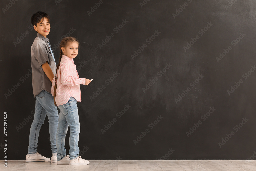 Little children with chalk piece near blackboard