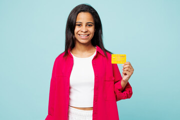 Wall Mural - Little fun kid teen girl of African American ethnicity wear pink shirt white t-shirt hold mock up of credit bank card isolated on plain pastel light blue cyan background. Childhood lifestyle concept.