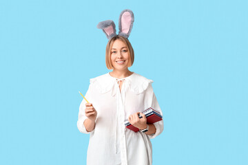 Wall Mural - Happy adult female manager in bunny ears with notebooks and pencil on blue background. Easter celebration